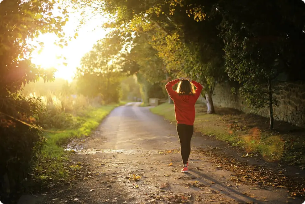 Foto de uma mulher iniciando uma caminhada em uma estrada refletida pelo sol
